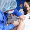 Imagen de una enfermera aplicando una vacuna a una mujer de mediana edad que usa tapabocas