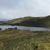 Laguna rodeada de vegetación natural y montañas bajo cielo nublado amplio