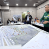 Autoridades distritales participan en simulación de manejo de emergencias alrededor de una mesa con mapas a gran escala, fichas de ubicación y material de planificación.