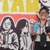 Mujer sonriente frente a un mural que ayudó a pintar.