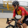 Paradeportista del Equipo Bogotá entrena ciclismo de pista en velódromo, usando casco y uniforme institucional rojo y amarillo, mientras pedalea sobre superficie inclinada con graderías metálicas al fondo.