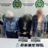 Tres mujeres capturadas en medio de dos policías. Los celulares recuperados están frente a ellas sobre una mesa.