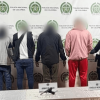 Cuatro capturados en medio de dos policías. El arma incautada está sobre una mesa.