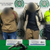 Dos capturados en medio de dos Policías. Sobre una mesa está el arma y los car