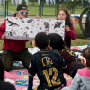 Imagen de dos personas mostranto un libro ilustrativo a niños en zona verde