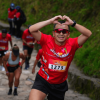 Participantes ascienden por el sendero de Monserrate, en primer plano un corredor con el número 1273 realiza un gesto de corazón con las manos mientras continúa el recorrido.