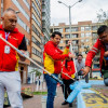 Grupo de trabajadores realiza labores de mantenimiento urbano pintando bordillos y superficies peatonales en espacio público, utilizando rodillos y pintura azul, con edificios residenciales y zona vial visibles al fondo.