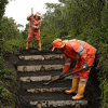 Foto que muestra dos personas con el uniforme de aguas de Bogotá instalando contrahuellas en un sendero ecológico