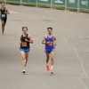 Grupo de atletas corre en la Media Maratón de Bogotá por una vía amplia durante competencia atlética urbana, con vallas metálicas a ambos lados y público observando desde el costado izquierdo
