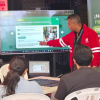 Foto que muestra personas sentadas y un señor señalando un televisor 