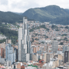 Vista panorámica del centro de Bogotá con edificios residenciales y empresariales de gran altura, cerros orientales cubiertos de vegetación y cielo nublado sobre la ciudad.