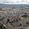 Vista aérea de Bogotá con extensa concentración de edificaciones, vías principales, cementerio central en primer plano y cielo cubierto de nubes sobre la ciudad.