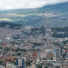 Panorámica de Bogotá con barrios densos, cerros verdes y cielo nublado fondo