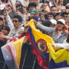 Asistentes a concierto en el parque Simón Bolívar permanecen frente a valla de seguridad del escenario, con banderas de Colombia visibles en primer plano.