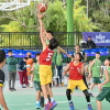 Jugadores disputan un balón bajo la canasta durante partido de baloncesto en los Juegos Intercolegiados, en una cancha cubierta con equipos identificados con uniformes rojos y verdes.