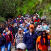Multitud numerosa avanza por un sendero peatonal estrecho rodeado de vegetación densa y árboles altos, en un entorno natural montañoso. Las personas caminan en fila y en grupos compactos