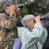 Grupo de personas observa aves con binoculares durante una jornada de avistamiento en un parque de Bogotá.