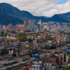 Vista panorámica de Bogotá con edificaciones residenciales y comerciales, vías principales y los cerros orientales al fondo bajo un cielo parcialmente nublado.