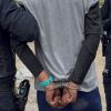 Hombre esposado, de espaldas, en medio de dos policías.