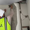 Persona con casco blanco y chaleco reflectivo con el logo de Bogotá inspecciona una columna y un muro interior con grietas visibles.