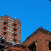 Edificaciones de ladrillo y torre de apartamentos en Bogotá, con vegetación en primer plano y cielo azul al fondo, en una escena urbana residencial.