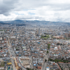 Vista aérea de Bogotá con alta concentración de edificaciones, corredores viales, zonas en construcción y montañas al fondo bajo un cielo nublado.