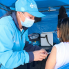 Foto que muestra a una persona del equipo de salud con uniforme azul aplicando una vacuna a una paciente mujer de pelo corto