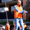 Foto que muestra un hombre con una carpeta en las manos y estudiantes sentados en el piso 