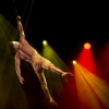 Imagen de un artista de circo en una puesta en escena al aire, de fondo se ven lices blancas y amarillas.