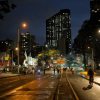 Ciclistas y peatones recorren una avenida iluminada durante la Ciclovía Nocturna de Bogotá, con edificios, comercio, alumbrado público y pavimento húmedo visibles en horario nocturno.