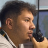 persona utilizando un radio portátil en centro de monitoreo de emergencias, con pantallas de información al fondo para el seguimiento de eventos en Bogotá.