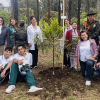 Grupo de personas participa en una jornada de siembra de árboles y arbustos en el Bosque Urbano San Carlos, junto a ejemplares recién plantados y rodeados de vegetación y árboles.