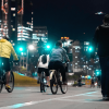 Personas en bicicleta y caminando durante la Ciclovía Nocturna en una vía de Bogotá iluminada por luces urbanas.
