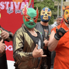 Cuatro luchadores con máscaras coloridas posan frente a un aviso del Festival de Verano durante una actividad de lucha libre en Bogotá.