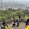 Personas acienden por el sendero de Monserrate con un fondo panorámico de la ciudad de Bogotá donde se observan edificios y zonas residenciales