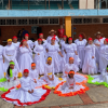 Grupo de personas con trajes folclóricos blancos y detalles de colores durante presentación artística en patio escolar de Bogotá.