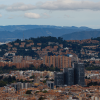 Vista panorámica de Bogotá con edificaciones residenciales y comerciales, zonas arborizadas y cerros al fondo bajo un cielo parcialmente nublado.
