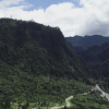 Vista aérea de los Cerros Orientales de Bogotá con laderas cubiertas de bosque, un valle atravesado por una vía y una quebrada.