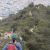 senderos del Parque de Montaña Entrenubes que es recorrido por personas en un día soleado. Al fondo de la imagen se observa una vista panorámica de Bogotá.