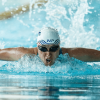 Persona practica natación estilo mariposa en una piscina de Bogotá, con gafas y gorro de natación mientras avanza entre salpicaduras de agua.