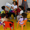 Niños en mesa redonda leyendo un libro con una profesora 
