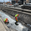 Foto que muestra dos personas con el uniforme de Aguas Bogotá limpiando un canal de agua 