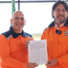 Foto que muestra dos personas sonriendo con un documento en la mano