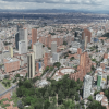 Vista aérea de un sector de Bogotá con edificios de gran altura, vías principales, zonas residenciales de alta densidad, áreas verdes y montañas al fondo bajo un cielo parcialmente nublado.