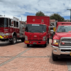 Vehículos del Cuerpo Oficial de Bomberos de Bogotá, entre ellos una máquina extintora, un camión de apoyo y una camioneta de emergencia, estacionados sobre una plazoleta de ladrillo.