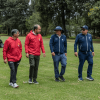 Cuatro personas caminan sobre el césped del campo de golf del Parque La Florida. Dos visten chaquetas rojas y dos chaquetas azules.