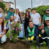 Grupo de personas posa alrededor de un arbusto con flores moradas recién sembrado en una zona verde.