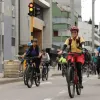 Grupo de personas en bicicleta recorre una vía urbana durante una jornada de Ciclovía. En primer plano se observa una persona con casco y chaleco reflectivo, mientras detrás avanzan más ciclistas por una avenida rodeada de edificios y señalización vial.