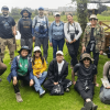 Grupo de 13 personas posa sobre una zona de césped del humedal Capellanía. Varias llevan binoculares, cámaras fotográficas y sombreros para observación de fauna.