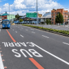 Carril preferencial para buses en la calle 63 de Bogotá, con un bus azul circulando por la vía, señalización vial pintada sobre el pavimento, separadores con vegetación y edificios al fondo.